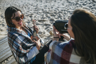 Lächelnde junge Frau spielt Ukulele, während ihr Freund mit der Videokamera aufnimmt - KIJF01320