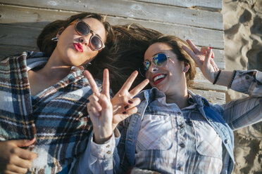 Zwei junge Frauen liegen auf der Holzpromenade und zeigen Siegeszeichen - KIJF01321