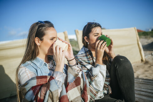 Zwei junge Frauen trinken Kaffee am Strand - KIJF01322