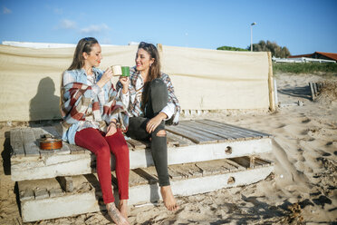 Two young women drinking coffee on the beach - KIJF01323