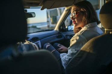 Junge Frau mit Sonnenbrille im Auto in der Abenddämmerung - KIJF01328