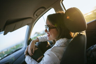 Junge Frau mit Sonnenbrille im Auto in der Abenddämmerung - KIJF01330