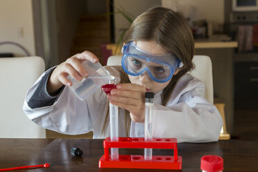 Mädchen mit Arbeitskittel und Schutzbrille bei der Arbeit mit einem Chemiebaukasten zu Hause - SARF03221