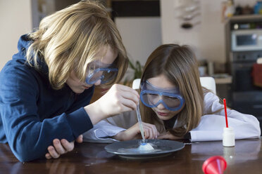 Zwei Kinder mit Schutzbrillen bei der Arbeit mit einem Chemiebaukasten zu Hause - SARF03225