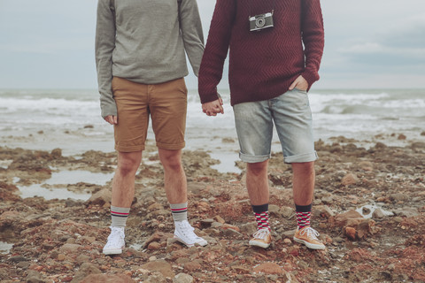 Young gay couple standing hand in hand on the beach, partial view stock photo
