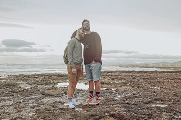 Glückliches junges schwules Paar am Strand stehend - RTBF00731