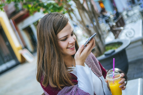 Junge Frau in Sevilla trinkt Fruchtsaft und singt auf ihrem Smartphone, lizenzfreies Stockfoto