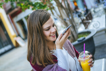 Young woman in Sevilla drinking fruit juice and sing smart phone - KIJF01338