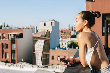 Junge Frau steht auf einem Dach in Brooklyn und schaut in die Ferne - GIOF02100