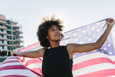 Young woman standing on rooftop holding US American flag - GIOF02119