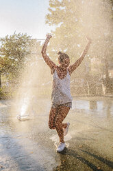 Junge Frau springt über den Wasserstrahl eines Springbrunnens - GIOF02132