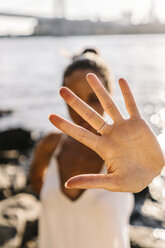 Young woman in Brooklyn standing at East River showing hand palm - GIOF02136