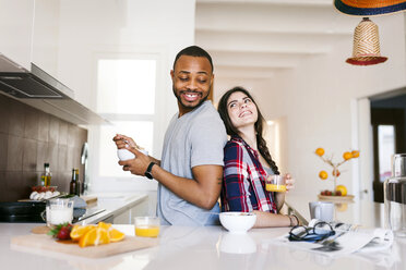 Young couple having breakfast in the kitchen, standing back to back - VABF01204