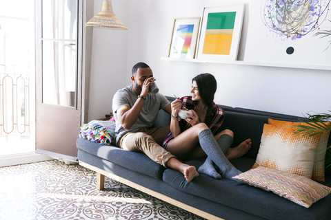 Junges Paar sitzt auf dem Sofa und frühstückt, lizenzfreies Stockfoto