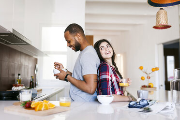 Young couple having breakfast in the kitchen, standing back to back - VABF01224