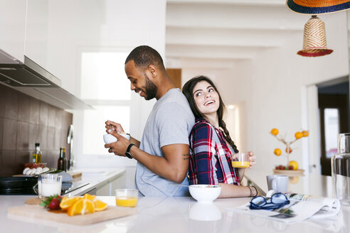 Young couple having breakfast in the kitchen, standing back to back - VABF01224