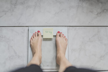 Woman standing on bathroom scales with sticky note of ideal weight - CHPF00371