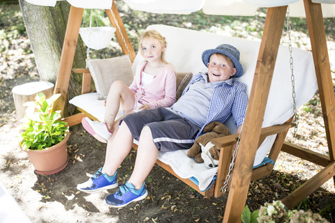 Schwester und Bruder sitzen in der Vordachschaukel, lizenzfreies Stockfoto