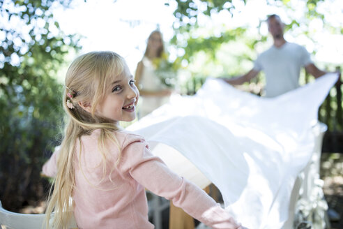 Lächelndes Mädchen mit ihren Eltern, die im Garten ein Tischtuch ausbreiten - WESTF22768