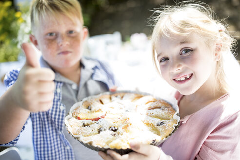 Porträt eines lächelnden Mädchens mit Bruder, das einen Kuchen im Freien hält - WESTF22777