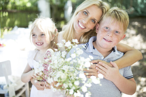 Lächelnde Mutter mit Muttertagsgeschenken, die ihre Kinder umarmen - WESTF22798