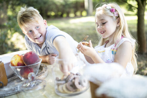 Schwester und Bruder essen Kuchen am Gartentisch - WESTF22807