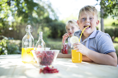 Schwester und Bruder trinken selbstgemachte Limonade am Gartentisch, lizenzfreies Stockfoto