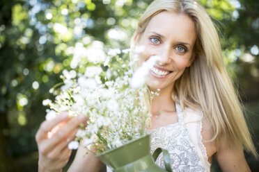 Smiling woman holding jug with flowers outdoors - WESTF22813