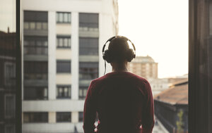 Mann mit Kopfhörern auf einem Balkon in der Stadt bei Sonnenuntergang - EPF00390