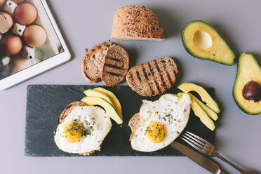 Breakfast with eggs, avovados and toasted bread on a table with digital tablet - GIOF02148