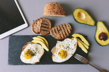 Frühstück mit Eiern, Avovados und getoastetem Brot auf einem Tisch mit digitalem Tablet - GIOF02150