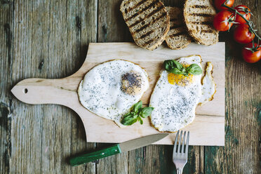 Eggs sunny side up on chopping board by tomatoes and toast - GIOF02168
