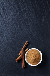 Bowl of cinnamon powder and cinnamon sticks on slate - CSF27973