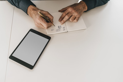 Mann zeichnet geometrische Formen in ein Notizbuch neben einem Tablet, lizenzfreies Stockfoto