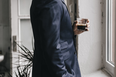 Geschäftsmann hält ein Glas Espresso am Fenster, lizenzfreies Stockfoto