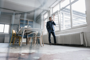 Reifer Geschäftsmann am Handy am Fenster im Büro - JOSF00700