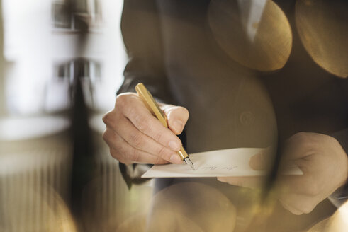 Hand of businessman writing with golden fountain pen on notepad - KNSF01134