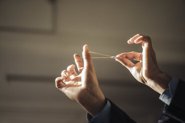 Hands of businessman aiming with rubber band and folded paper - KNSF01139