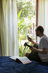 Mann mit Gitarre und Mobiltelefon auf dem Bett sitzend - KNTF00666