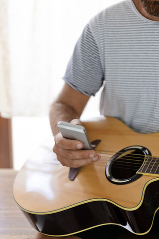 Nahaufnahme eines Mannes mit Gitarre und Mobiltelefon, lizenzfreies Stockfoto