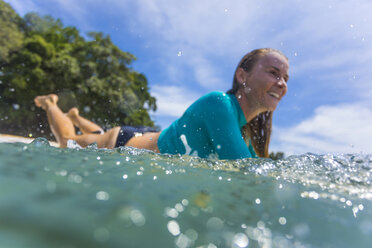 Indonesien, Java, lächelnde Frau auf Surfbrett auf dem Meer liegend - KNTF00672
