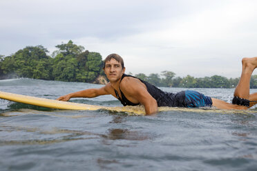 Indonesia, Java, man lying on surfboard on the sea - KNTF00681