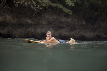 Indonesia, Java, man lying on surfboard on the sea - KNTF00697