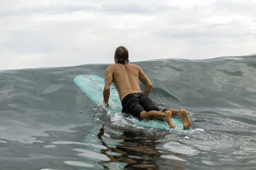 Indonesia, Java, man lying on surfboard on the sea - KNTF00701