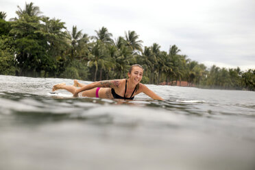 Indonesien, Java, lächelnde Frau auf Surfbrett auf dem Meer liegend - KNTF00705