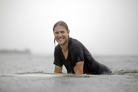 Indonesia, Java, smiling man on surfboard on the sea stock photo