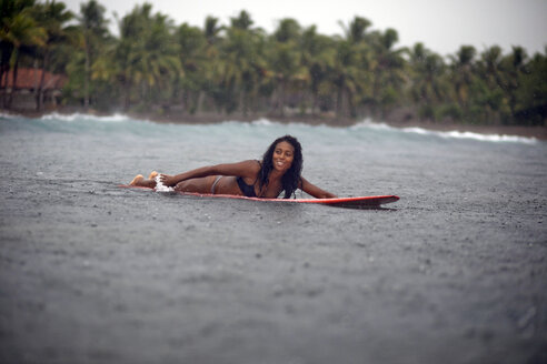 Indonesien, Java, Frau auf Surfbrett liegend auf dem Meer im Regen - KNTF00721