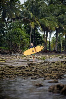 Indonesien, Java, Mann mit Surfbrett an der Küste - KNTF00724