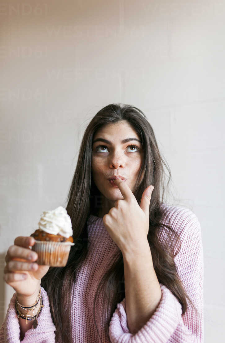 Young woman eating a cup cake with whipped cream, licking finger stock photo