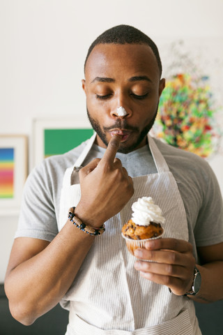 Young man eating a cup cake with whipped cream, licking finger stock photo